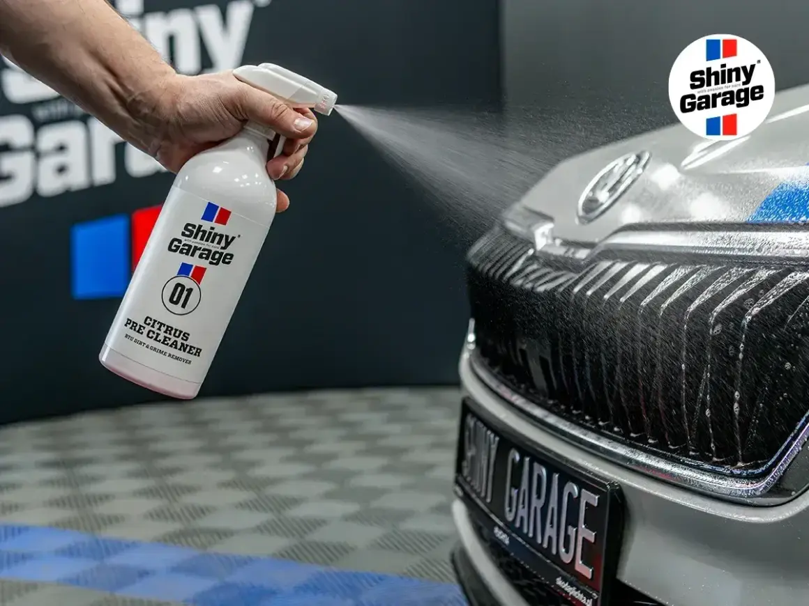Ręka rozpyla preparat Shiny Garage Citrus Pre Cleaner na grill samochodu, rozpoczynając jego mycie.