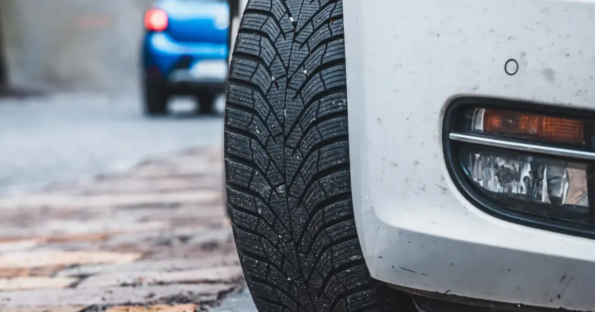 Białe auto z oponami zimowymi na mokrej nawierzchni. Niebezpieczna jazda na letnich oponach w zimie to ryzyko.
