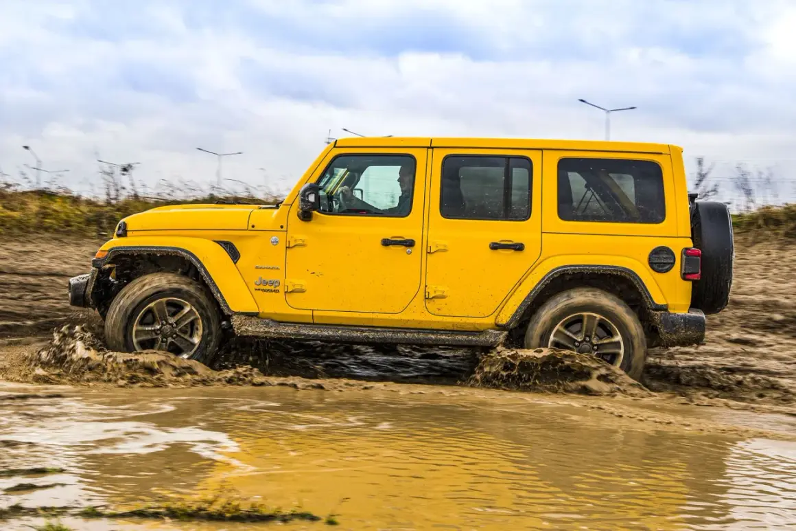 Żółty Jeep Wrangler Sahara pokonuje błotniste rozlewiska, pokazując swoje możliwości terenowe 4x4.