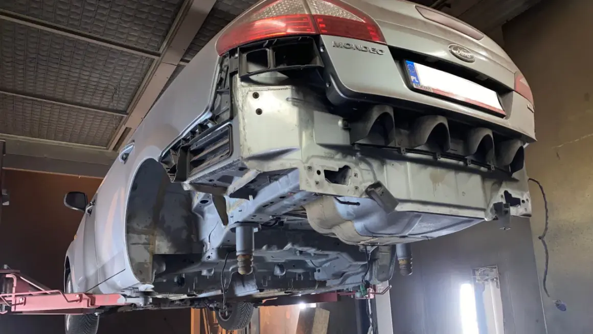 Ford Mondeo na podnośniku, przygotowany do piaskowania podwozia. Widać gołe elementy konstrukcyjne i usunięty zderzak.