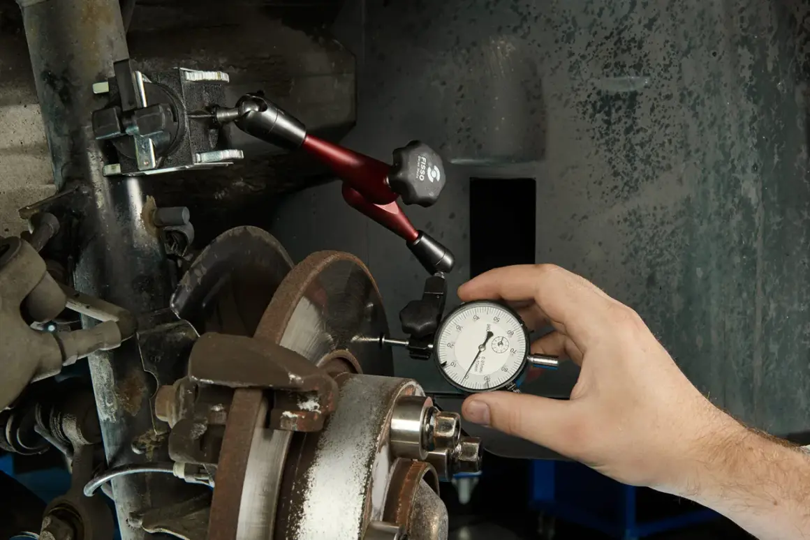 Mechanik mierzy bicie tarczy hamulcowej, aby zdiagnozować drgania kierownicy przy hamowaniu.