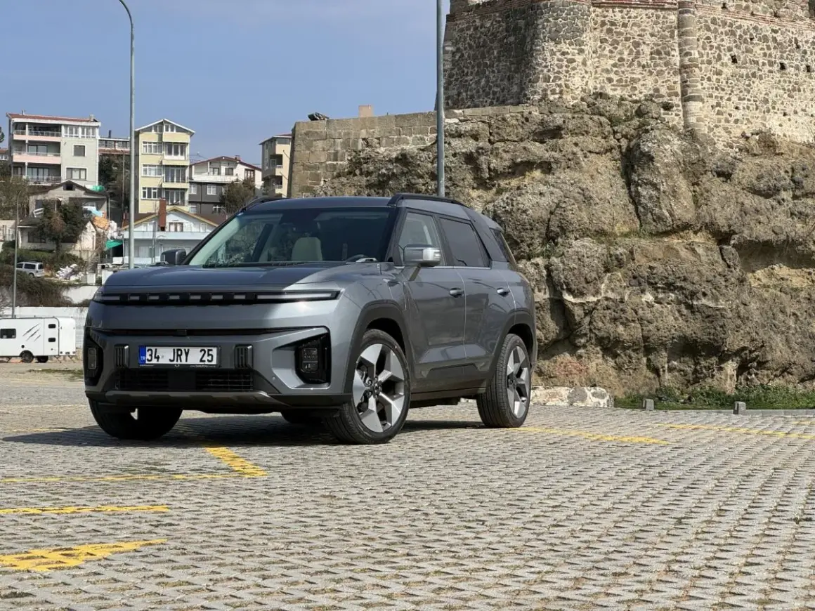 Nowy SsangYong elektryczny SUV stoi na parkingu przed kamiennym murem.