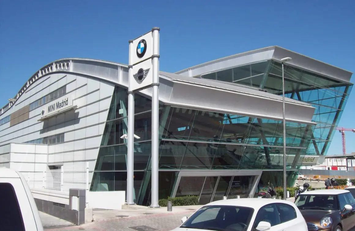 Nowoczesny salon MINI Madrid z logo BMW. W tle widać budynek i dźwig budowlany, a przed nim zaparkowane samochody, gotowe do akcje przywoławcze BMW.