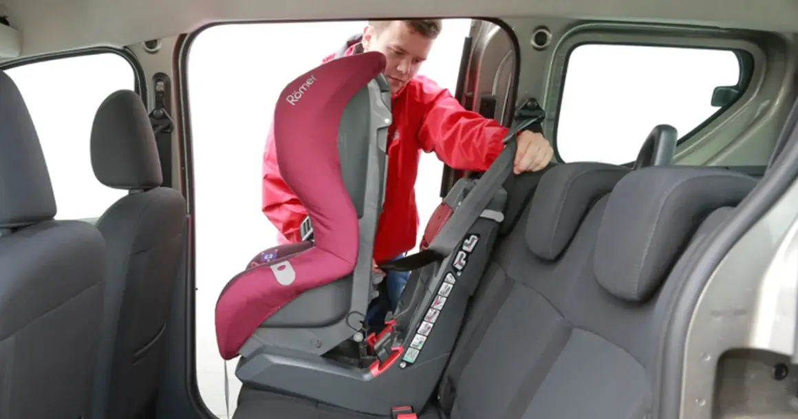 Mężczyzna montuje fotelik dziecięcy. Sprawdź, jak sprawdzić, czy samochód ma isofix, patrząc na zaczepy fotelika.
