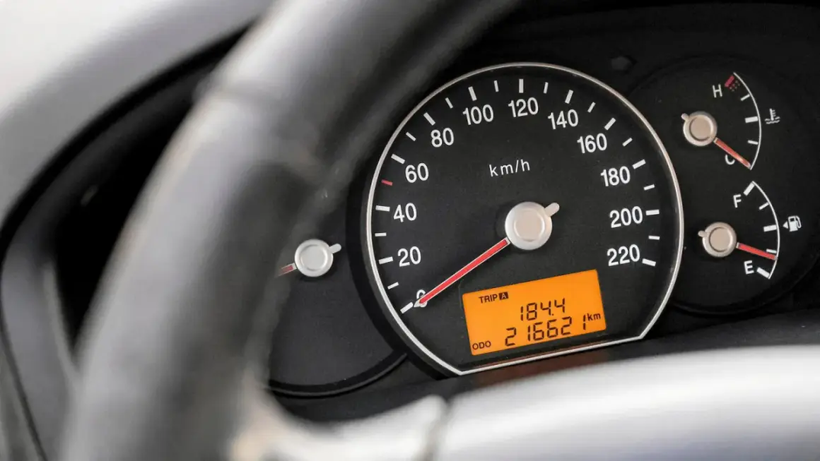 Zbliżenie na deskę rozdzielczą samochodu. Widoczny prędkościomierz, wskaźnik paliwa i temperatury. Cyfrowy wyświetlacz pokazuje przebieg 216621 km.