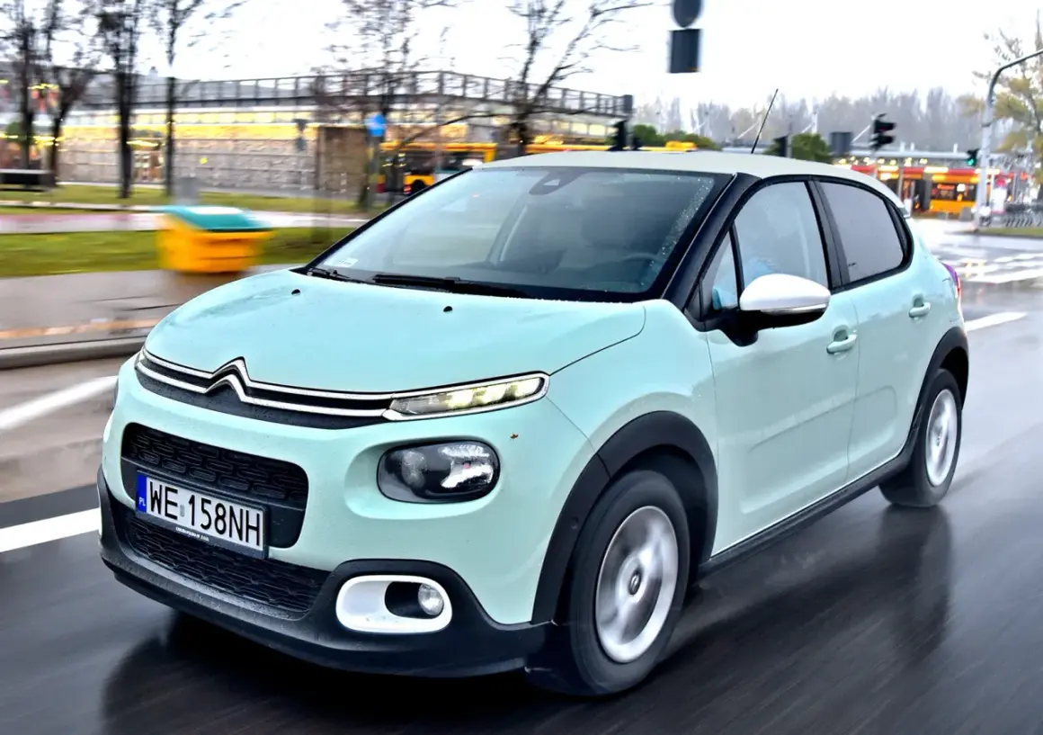 Jasnozielony Citroën C3, jeden z francuskich marek samochodów, jedzie po mokrej drodze.