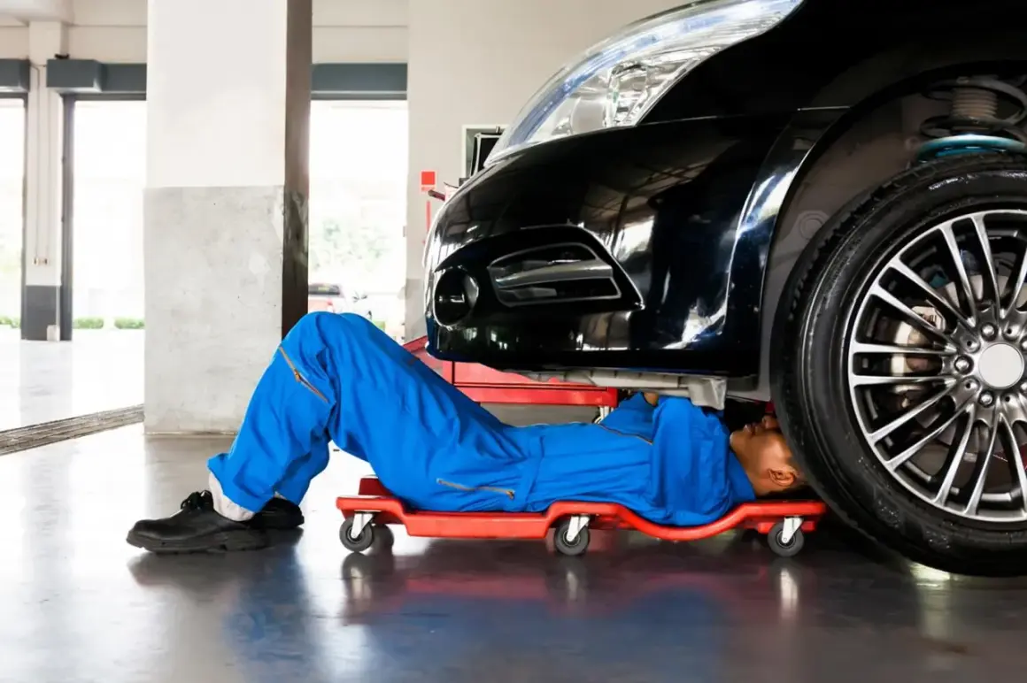 Mechanik pod czarnym autem szuka czujnika położenia wału w Peugeot 207.