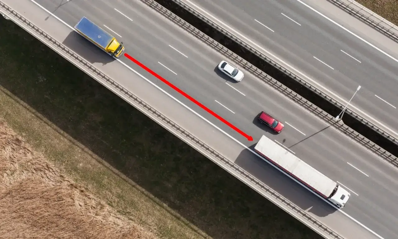 Czerwona strzałka pokazuje niebezpieczny manewr brake check wykonany przez czerwony samochód przed białą ciężarówką na autostradzie.