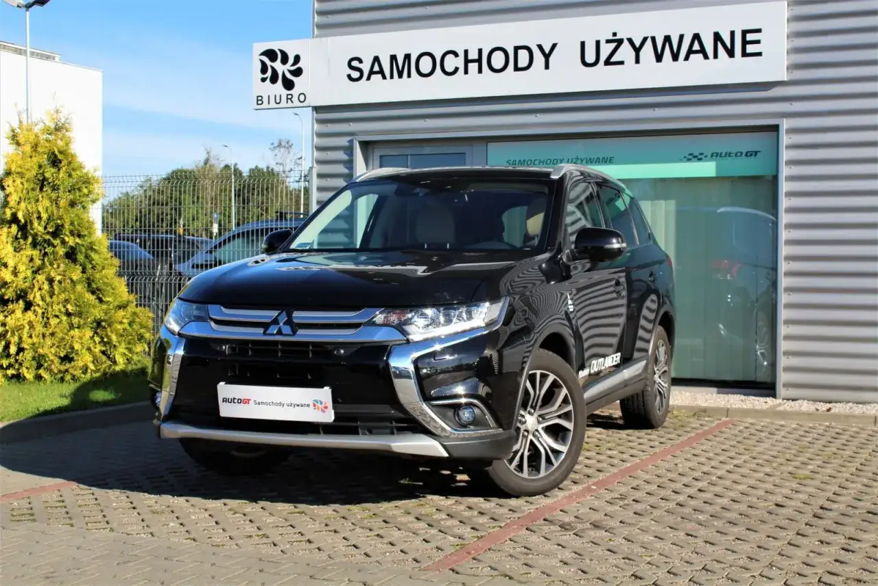Czarny Mitsubishi Outlander z przedłużoną gwarancją, zaparkowany przed salonem samochodów używanych.
