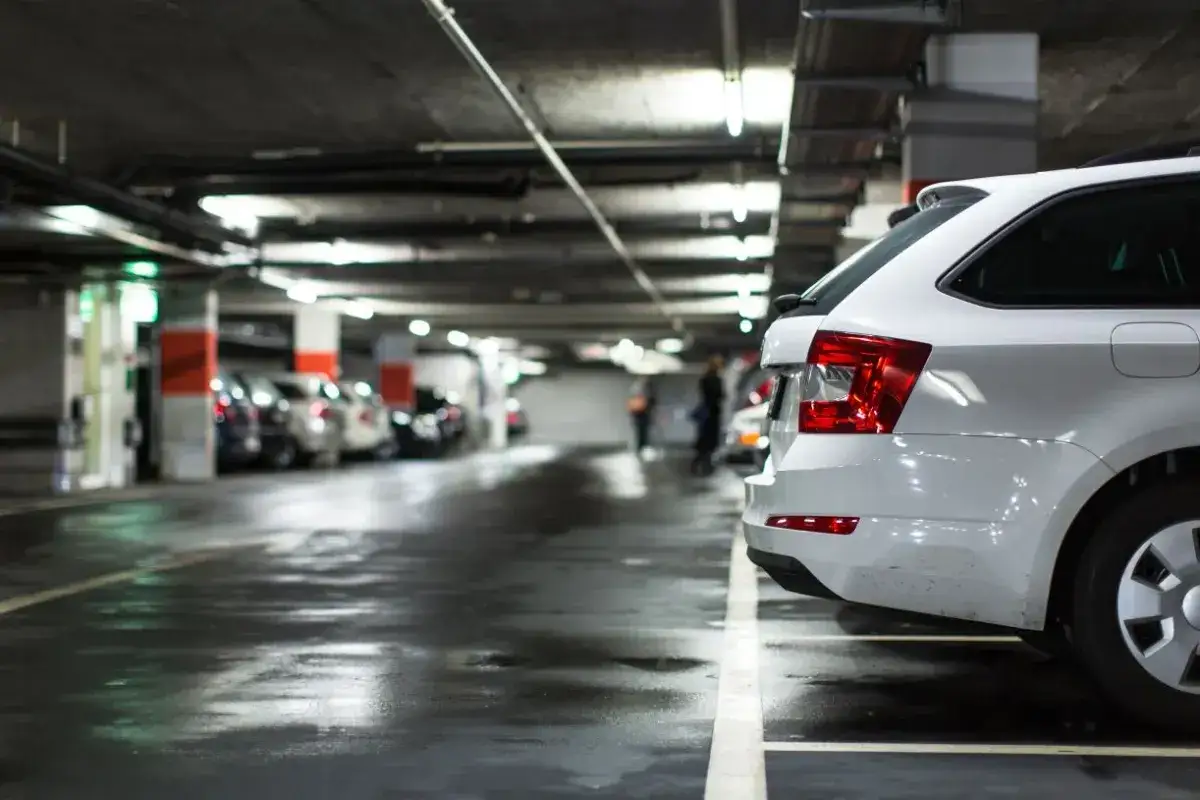 Biały samochód na parkingu podziemnym. Rozważasz wynajem samochodu od osoby prywatnej a podatek?