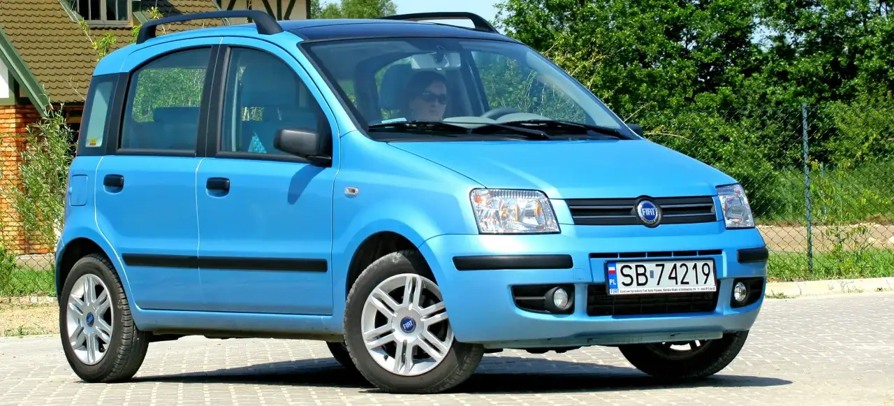 Błękitny Fiat Panda, pierwszy samochód z panoramicznym dachem, zaparkowany na kostce brukowej.