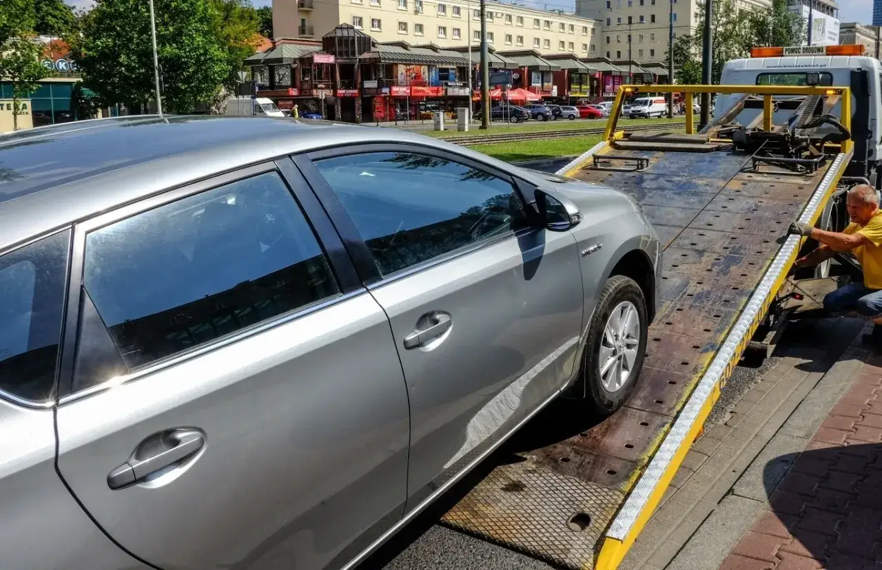 Srebrny samochód na lawecie. Kierowca w żółtej koszulce zabezpiecza pojazd. Nowe kary za jazdę po alkoholu mogą prowadzić do takich widoków.