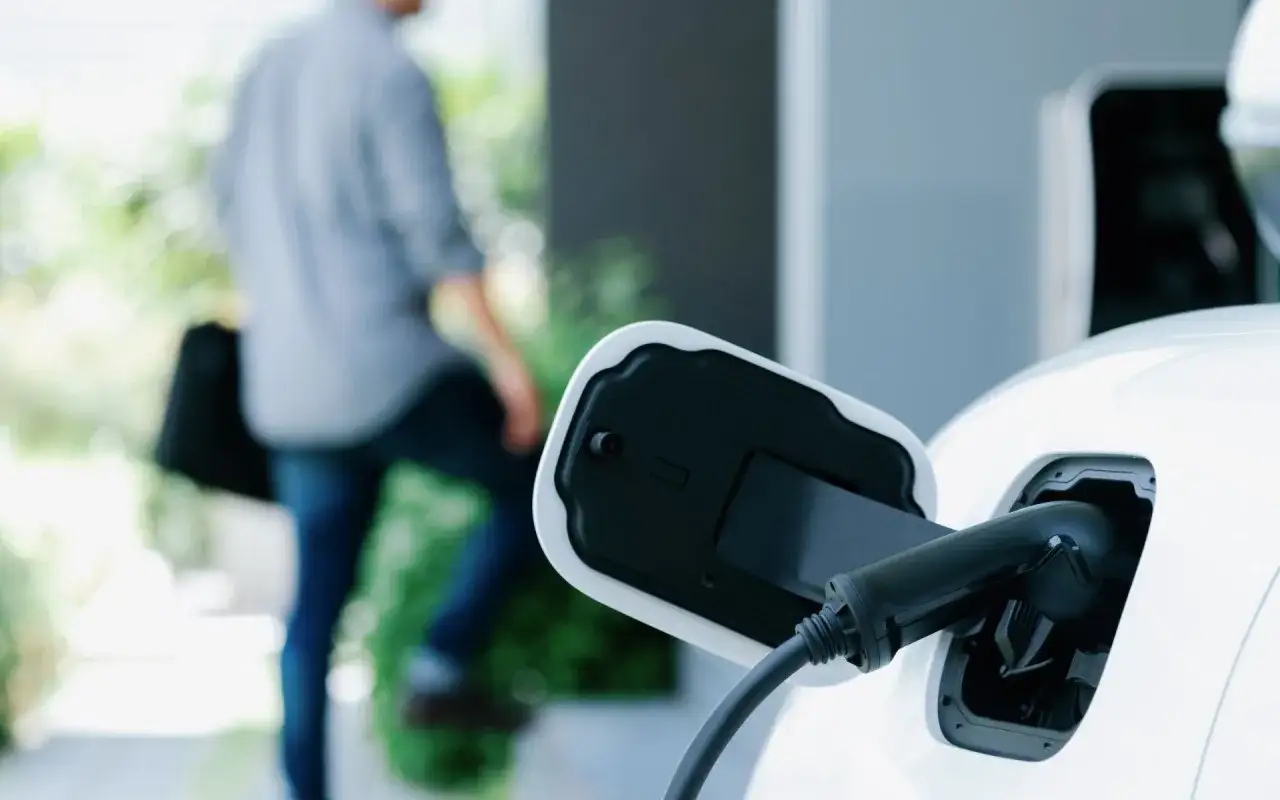 Ładowanie hybrydy plug-in. Wtyczka podłączona do samochodu, a w tle widać sylwetkę osoby.