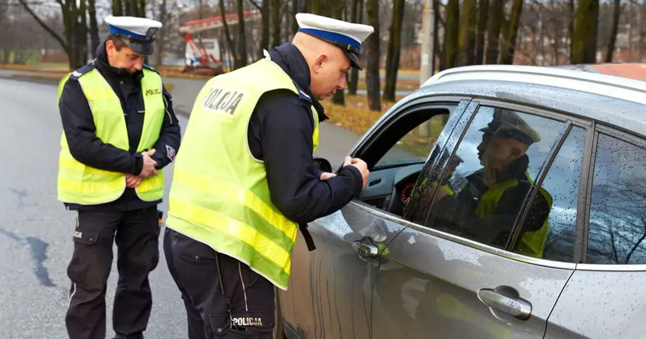 Policjanci zatrzymali kierowcę za przekroczenie prędkości. Jeden z funkcjonariuszy rozmawia z kierowcą przez otwarte okno samochodu.