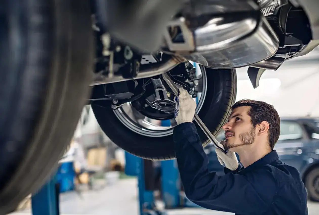 Mechanik w rękawiczkach pracuje nad zawieszeniem w samochodzie, używając klucza.
