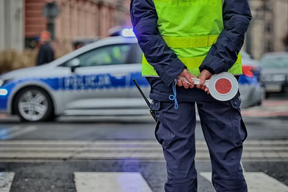 Policjant w kamizelce odblaskowej z lizakiem w dłoniach, obok radiowóz. Nowe przepisy drogowe w praktyce.