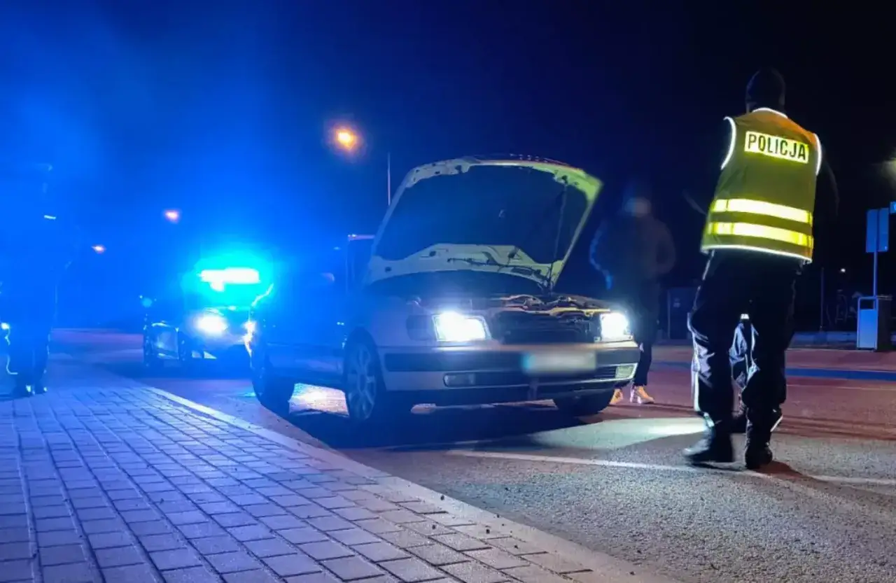 Policja przerwała nielegalne wyścigi. Samochód z otwartą maską, policyjne światła i funkcjonariusz w kamizelce odblaskowej.