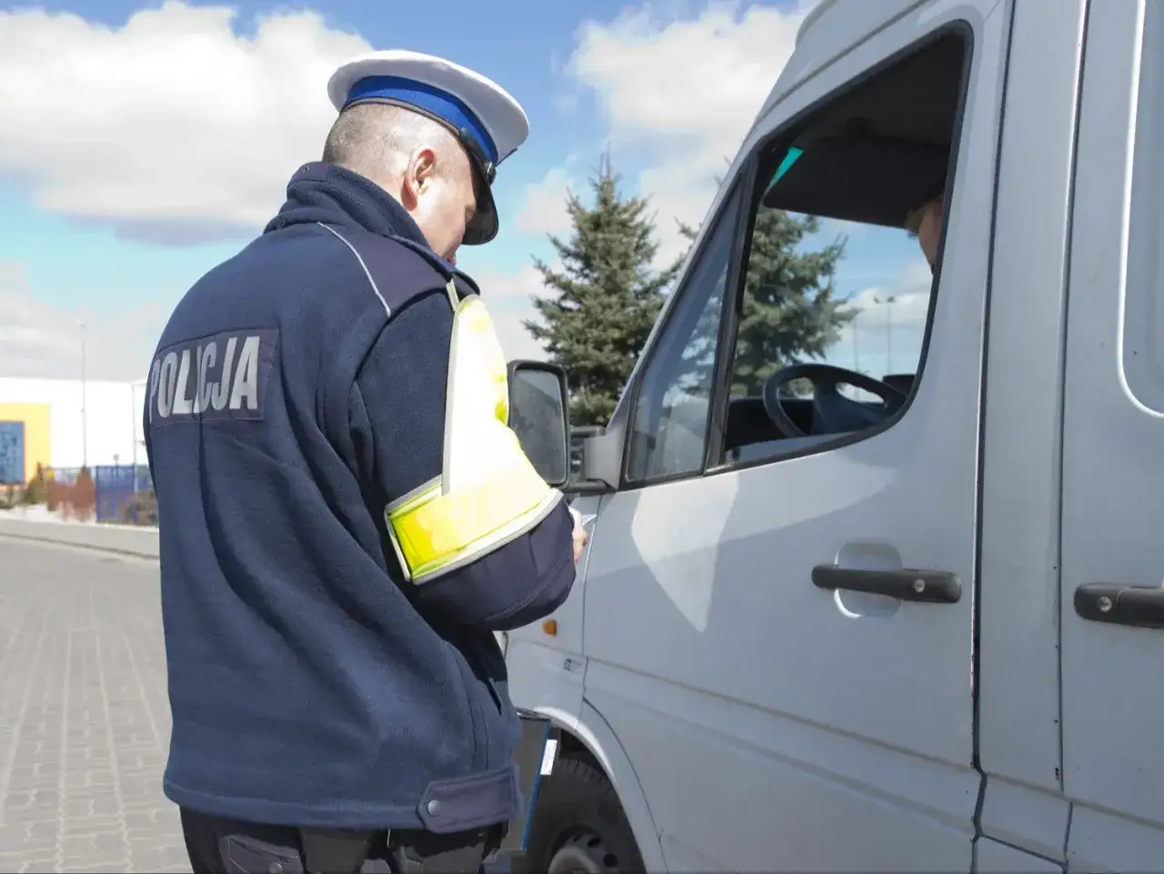 Policjant kontroluje kierowcę białej furgonetki. Kierowca może mieć rekord punktów karnych.