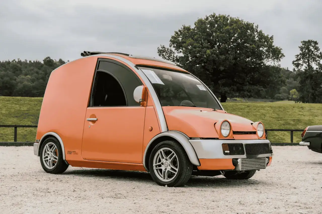 Pomarańczowy Nissan S Cargo, często uznawany za najbrzydszy samochód na świecie, z podwójnym wydechem na dachu.
