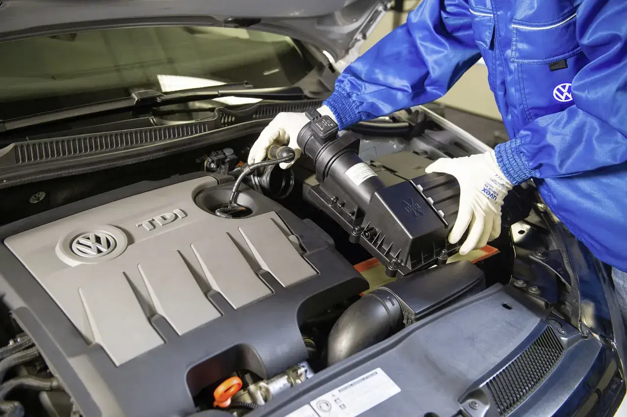 Mechanik w białych rękawiczkach wymienia element układu dolotowego w silniku TDI. Szarpanie na ciepłym silniku benzyna może być związane z tym elementem.