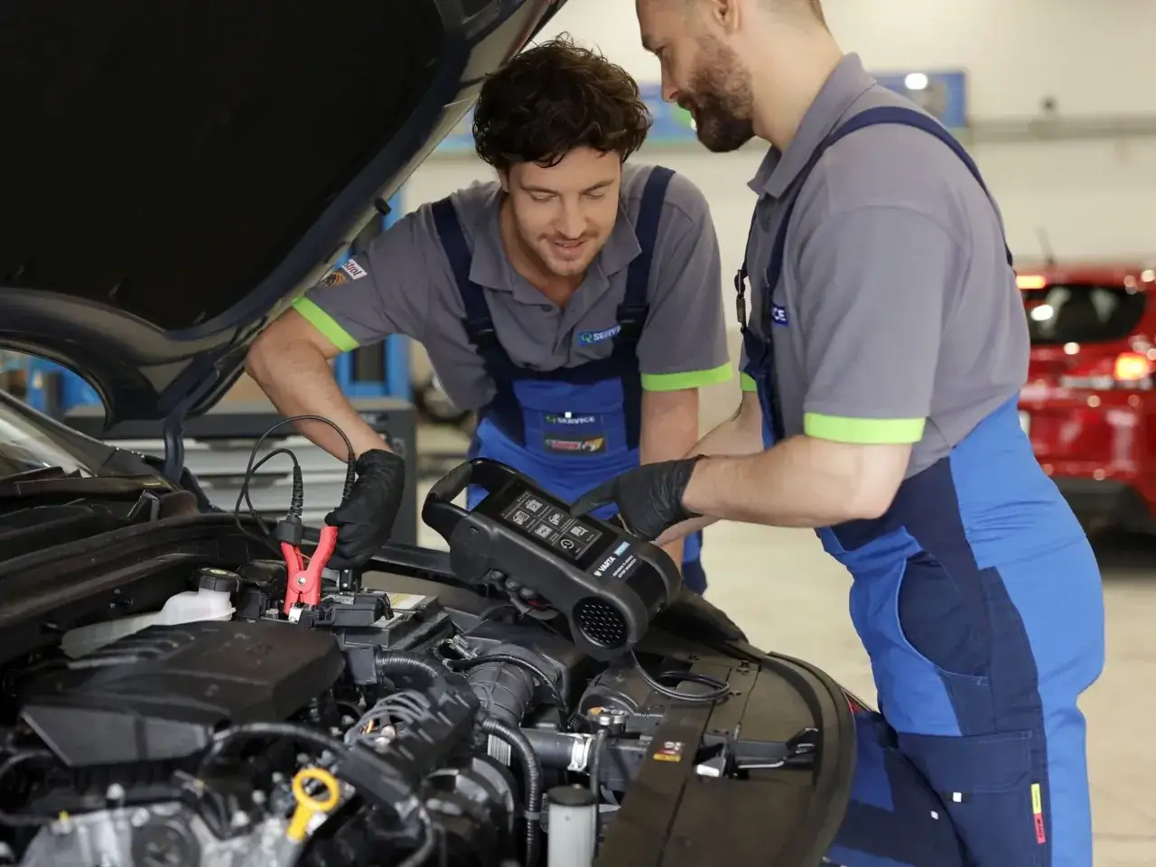 Mechanicy diagnozują problem szarpania silnika za pomocą testera akumulatora.