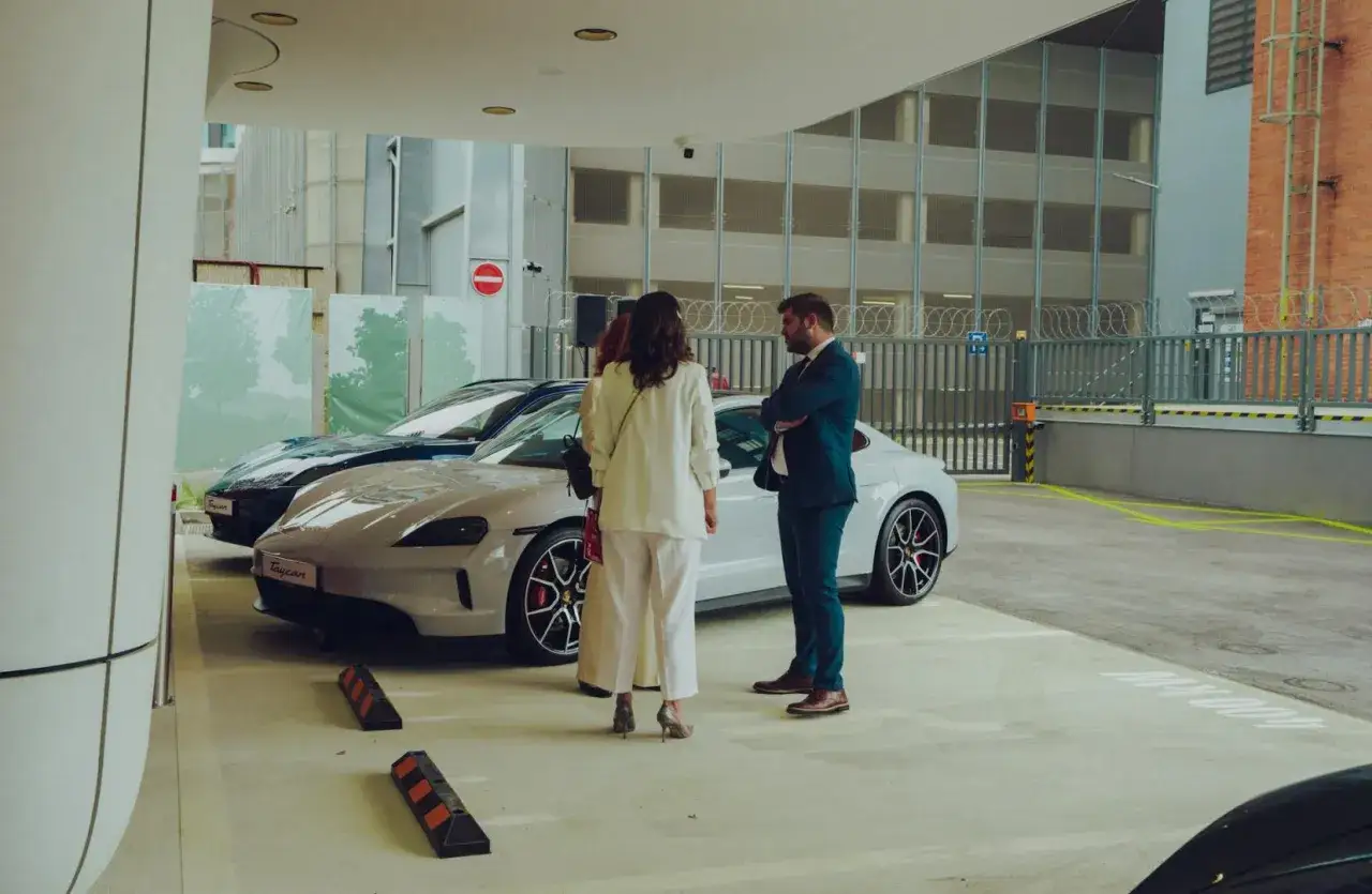 Para ogląda Porsche Taycan, idealny samochód po leasingu. Elegancko ubrani dyskutują o jego zaletach.