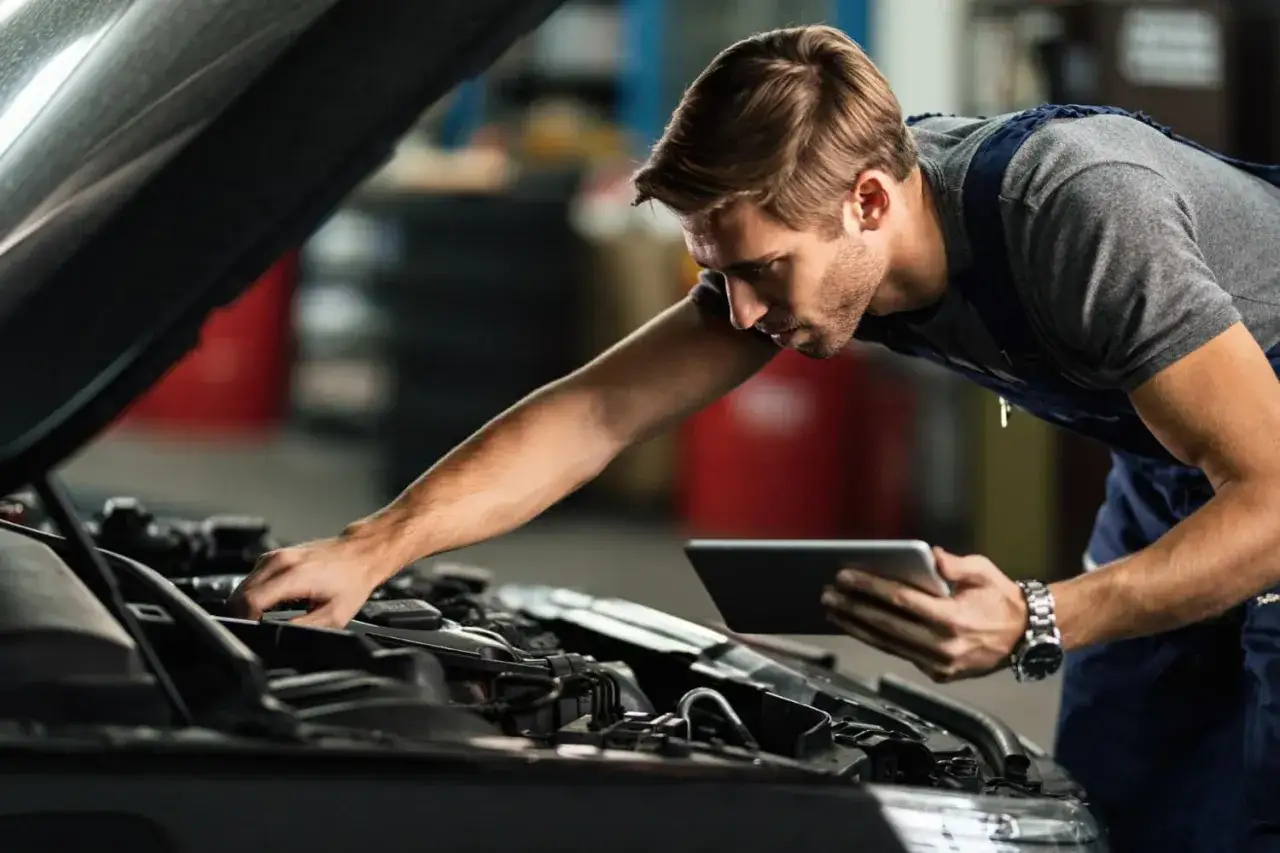 Mechanik z tabletem w ręku wykonuje pierwszy przegląd gwarancyjny samochodu, sprawdzając silnik.
