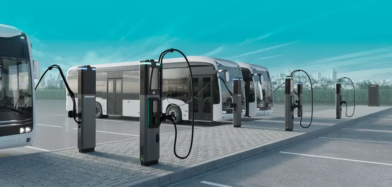 Nowoczesne, białe autobusy elektryczne podłączone do stacji ładowania na tle miasta.