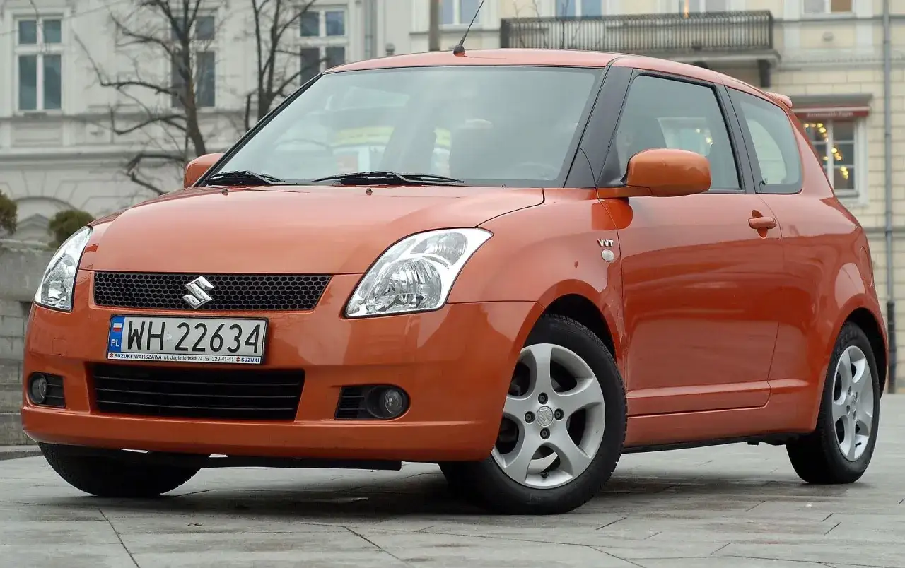 Pomarańczowy Suzuki Swift, pierwszy samochód z salonu, stoi na ulicy.