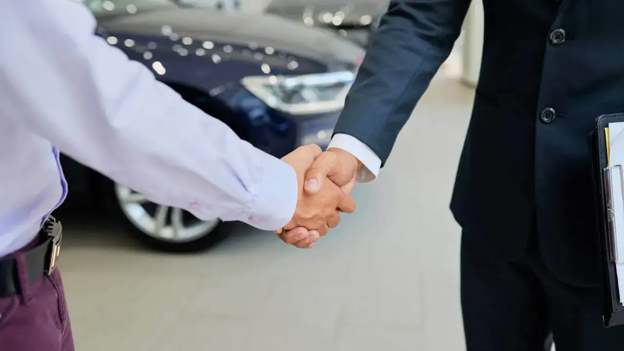 Uścisk dłoni między sprzedawcą a klientem przed nowym samochodem. Dowiedz się, jak sprzedać auto w leasingu.