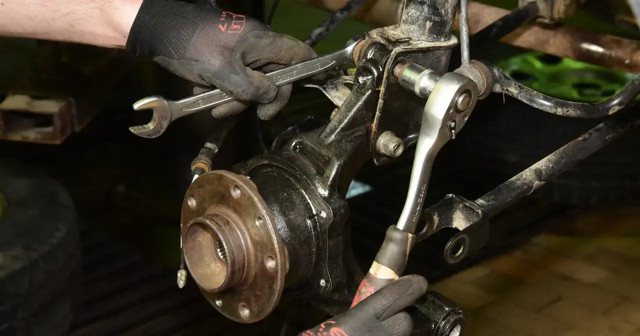 Mechanik w rękawiczkach używa kluczy do wymiany łożyska w samochodzie.