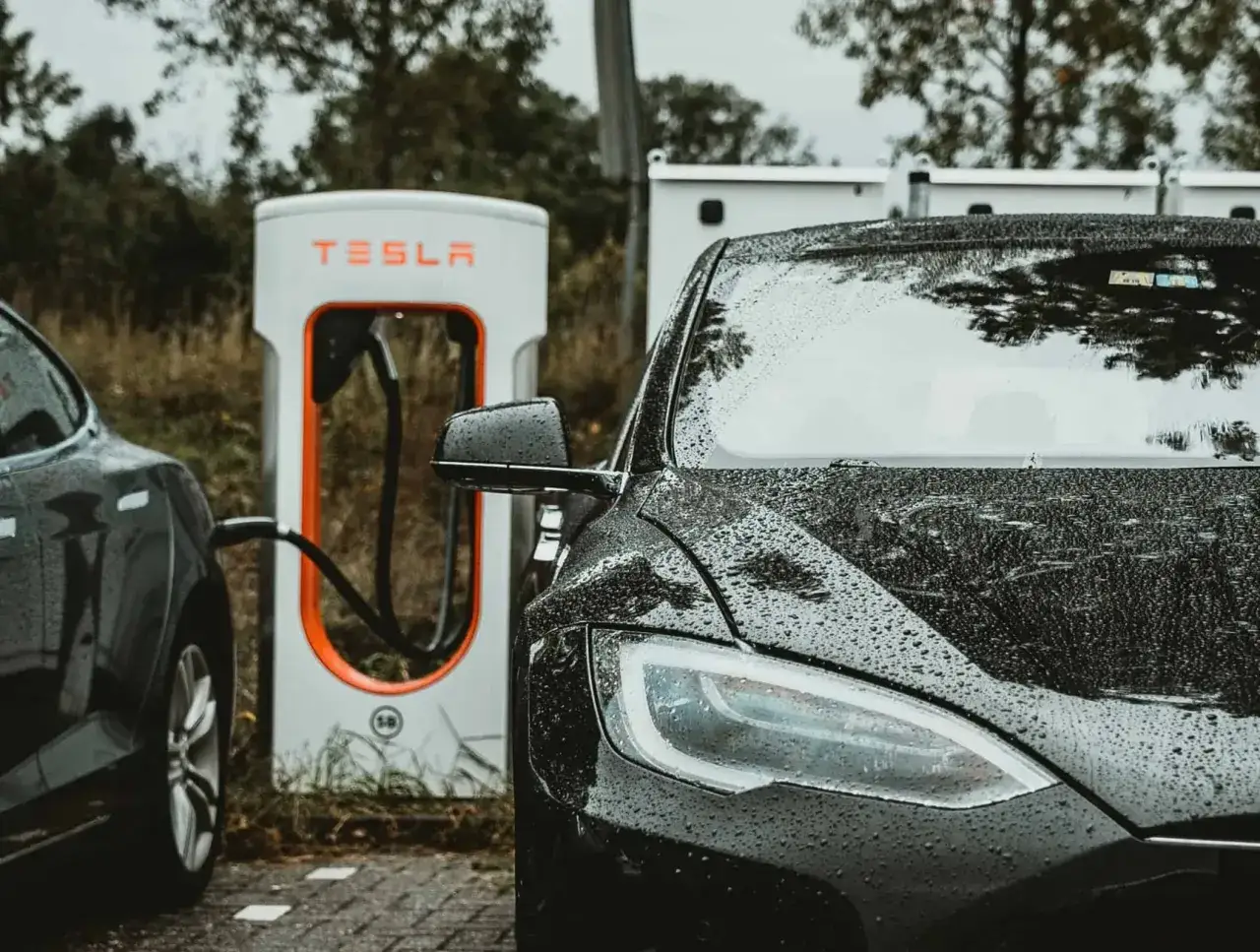 Czarny Tesla hybryda ładuje się na stacji Tesla Supercharger w deszczowy dzień.