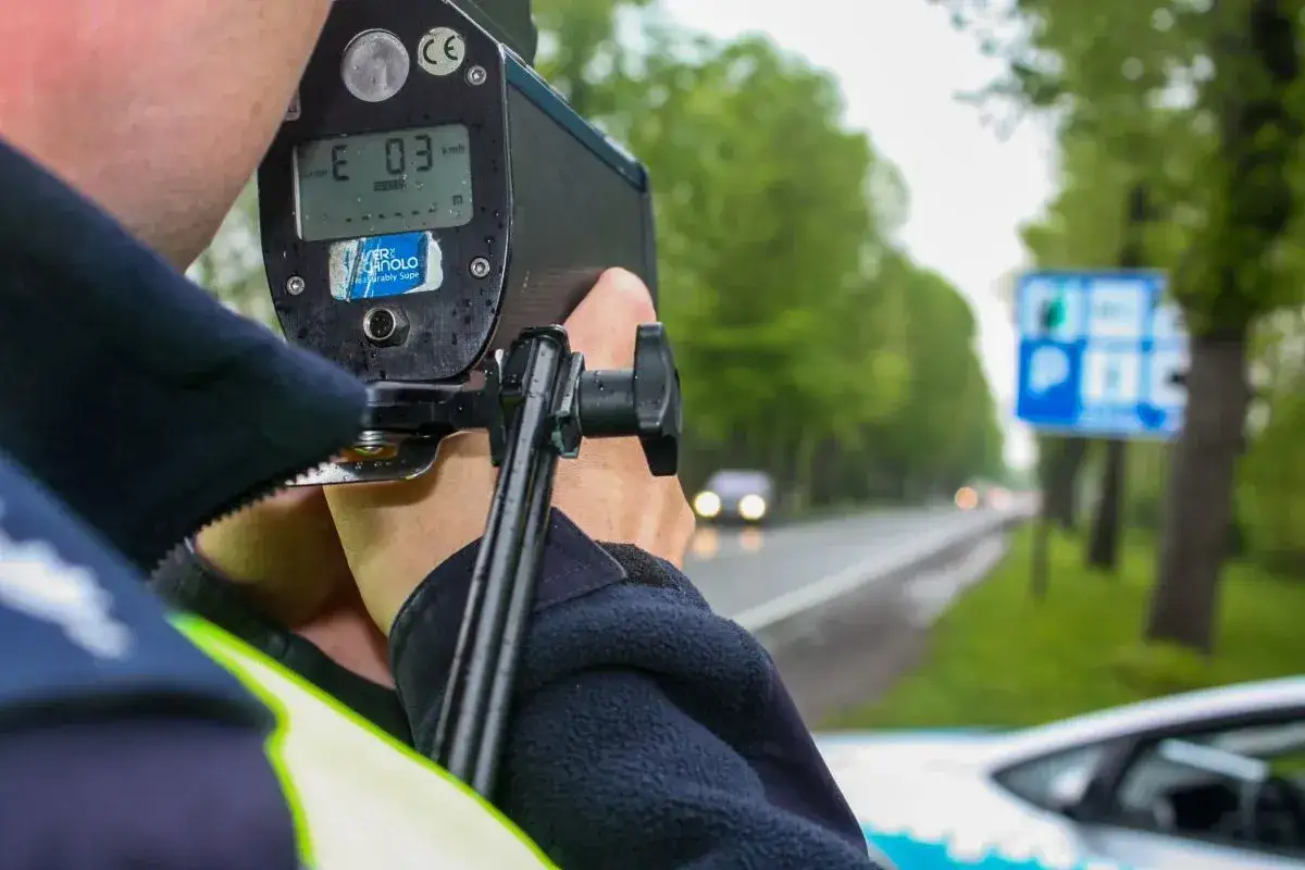 Policjant prowadzi pomiar prędkości w nocy. Na drodze widać samochody i znaki drogowe.