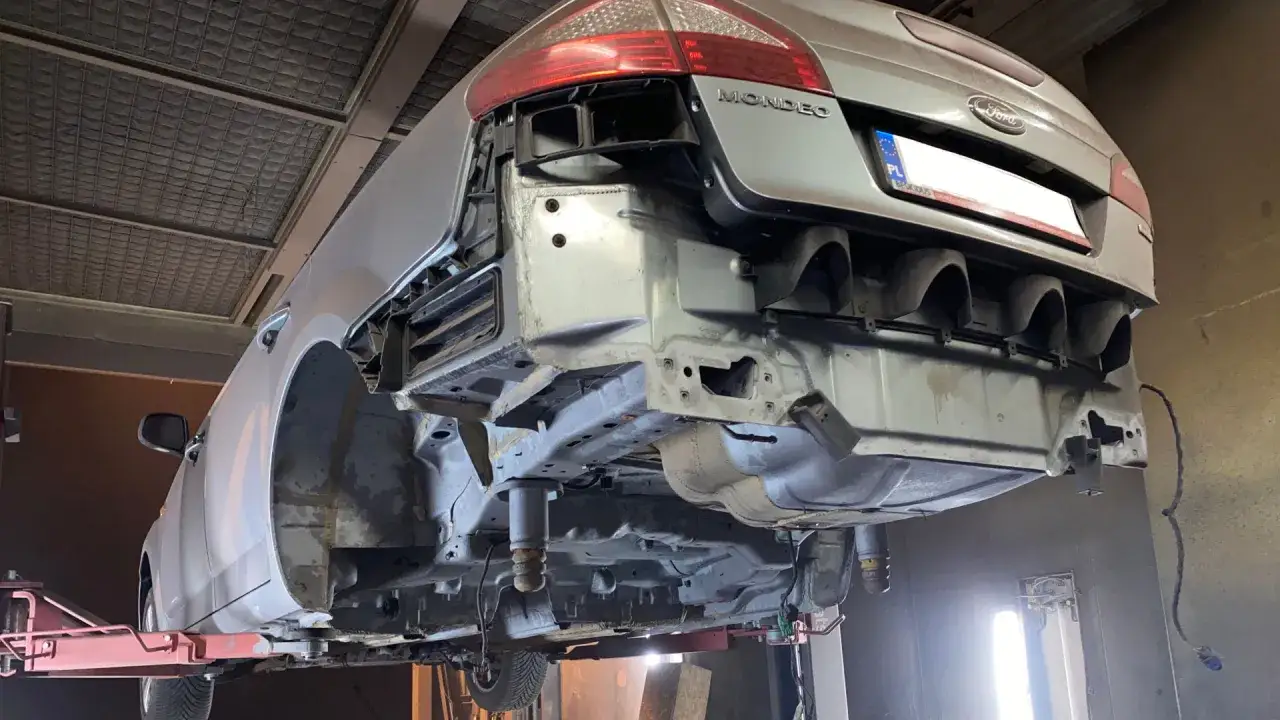 Samochód Ford Mondeo na podnośniku, przygotowany do piaskowania podwozia. Widać odsłonięte elementy konstrukcyjne i tylny zderzak.