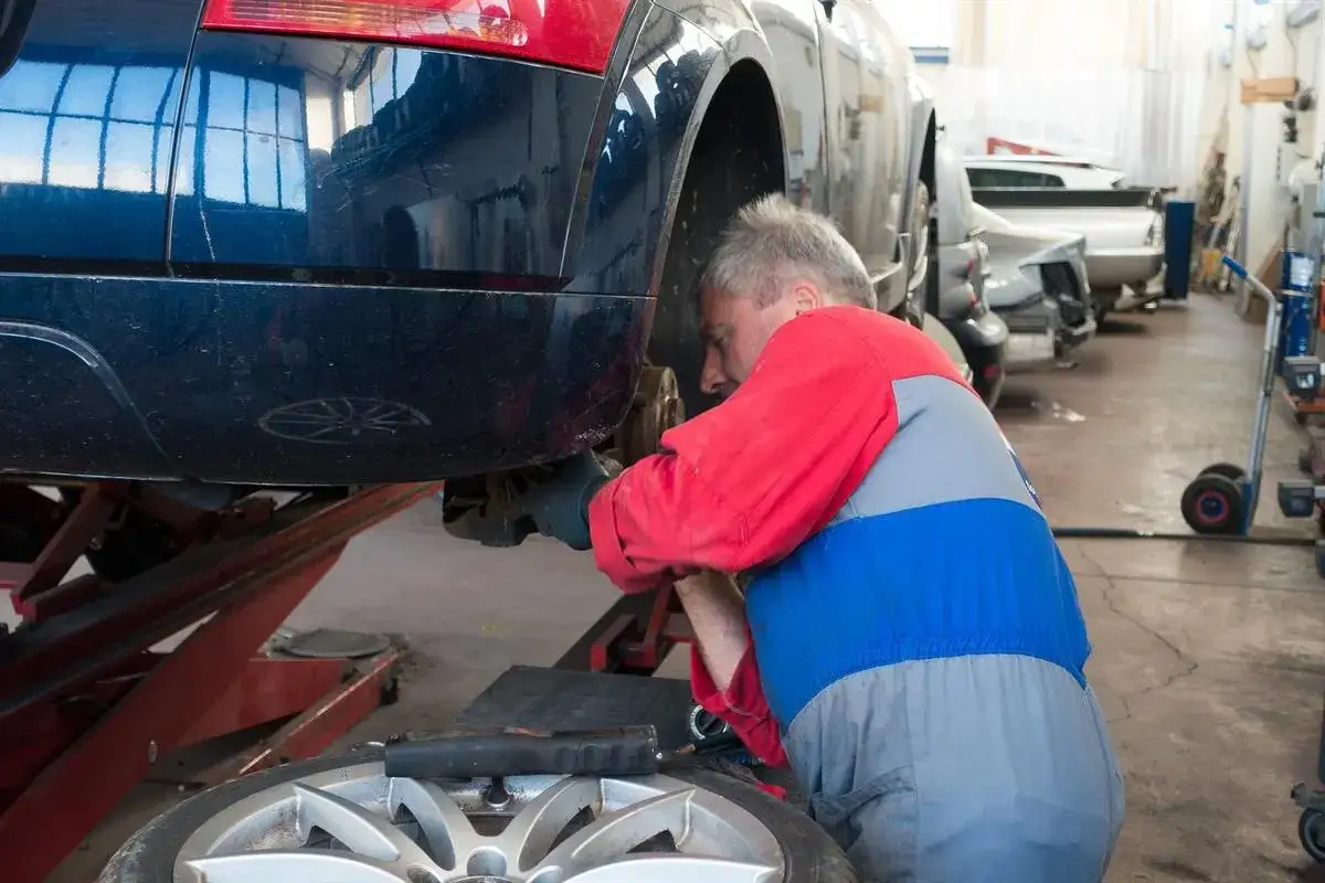 Mechanik naprawia samochód, który nagle zgasł podczas jazdy. Auto stoi na podnośniku, a mechanik pracuje przy tylnym zawieszeniu.