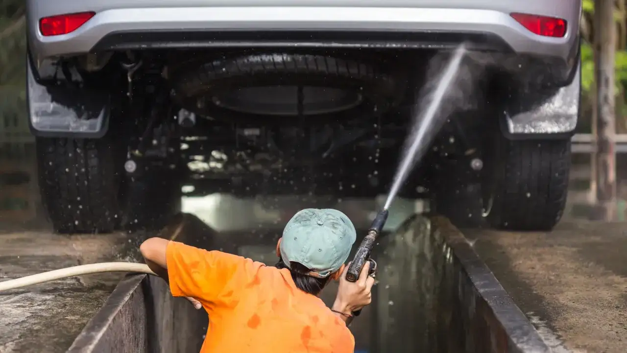 Osoba w pomarańczowej koszulce myje auto myjką ciśnieniową. Czy można myć auto w zimie? Tak, jeśli chcesz utrzymać je w czystości.