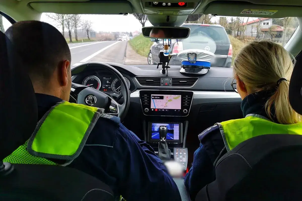 Policjanci w radiowozie patrolują drogę. Kierowca bez prawa jazdy może spodziewać się mandatu.