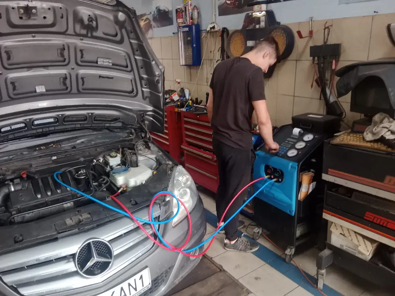 Mechanik diagnozuje usterki klimatyzacji samochodowej, podłączając urządzenie do silnika Mercedesa.