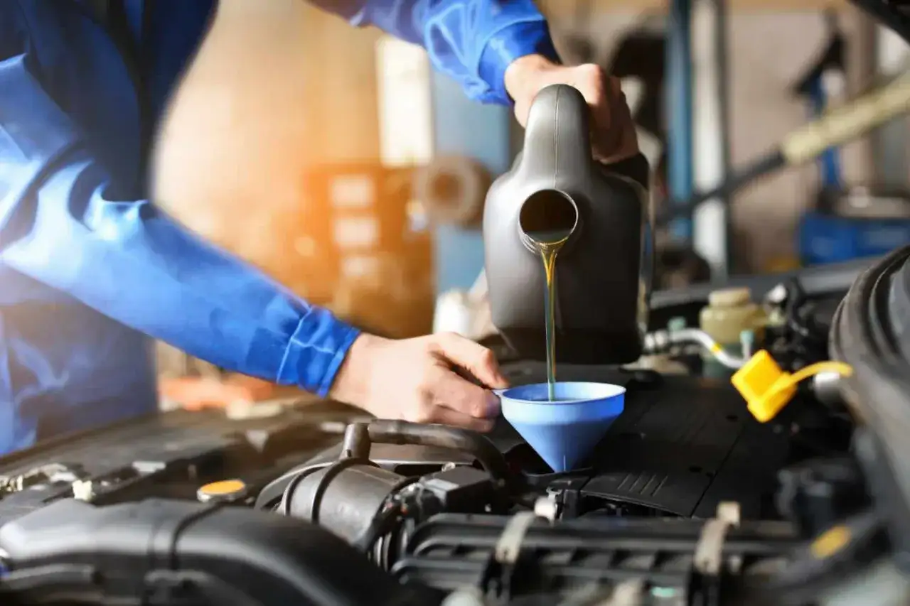 Mechanik w niebieskim kombinezonie nalewa olej do silnika, używając lejka. To ważny element dbania o auto, podobnie jak wybór odpowiednich filtrów przy wymianie oleju.