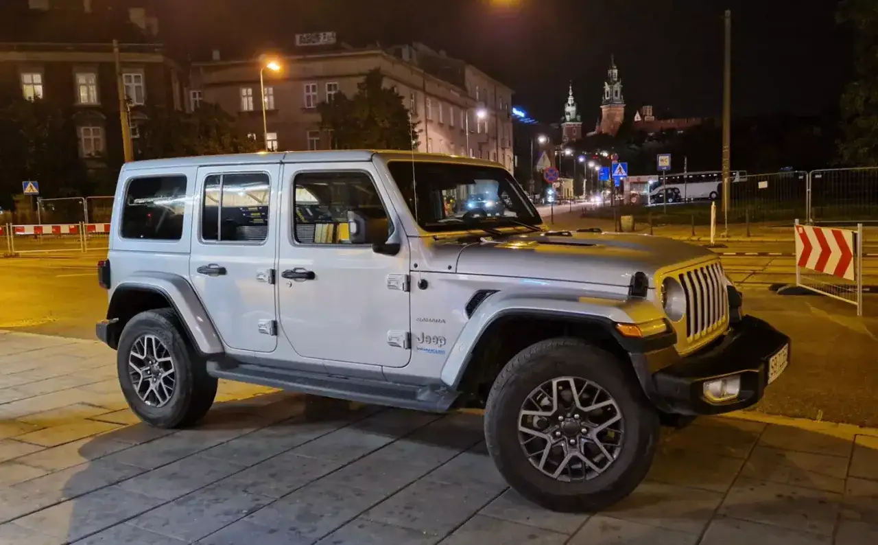Srebrny Jeep Wrangler Sahara, gotowy na nowe przygody po zakończeniu leasingu. W tle nocne miasto z oświetlonymi budynkami i zamkiem.