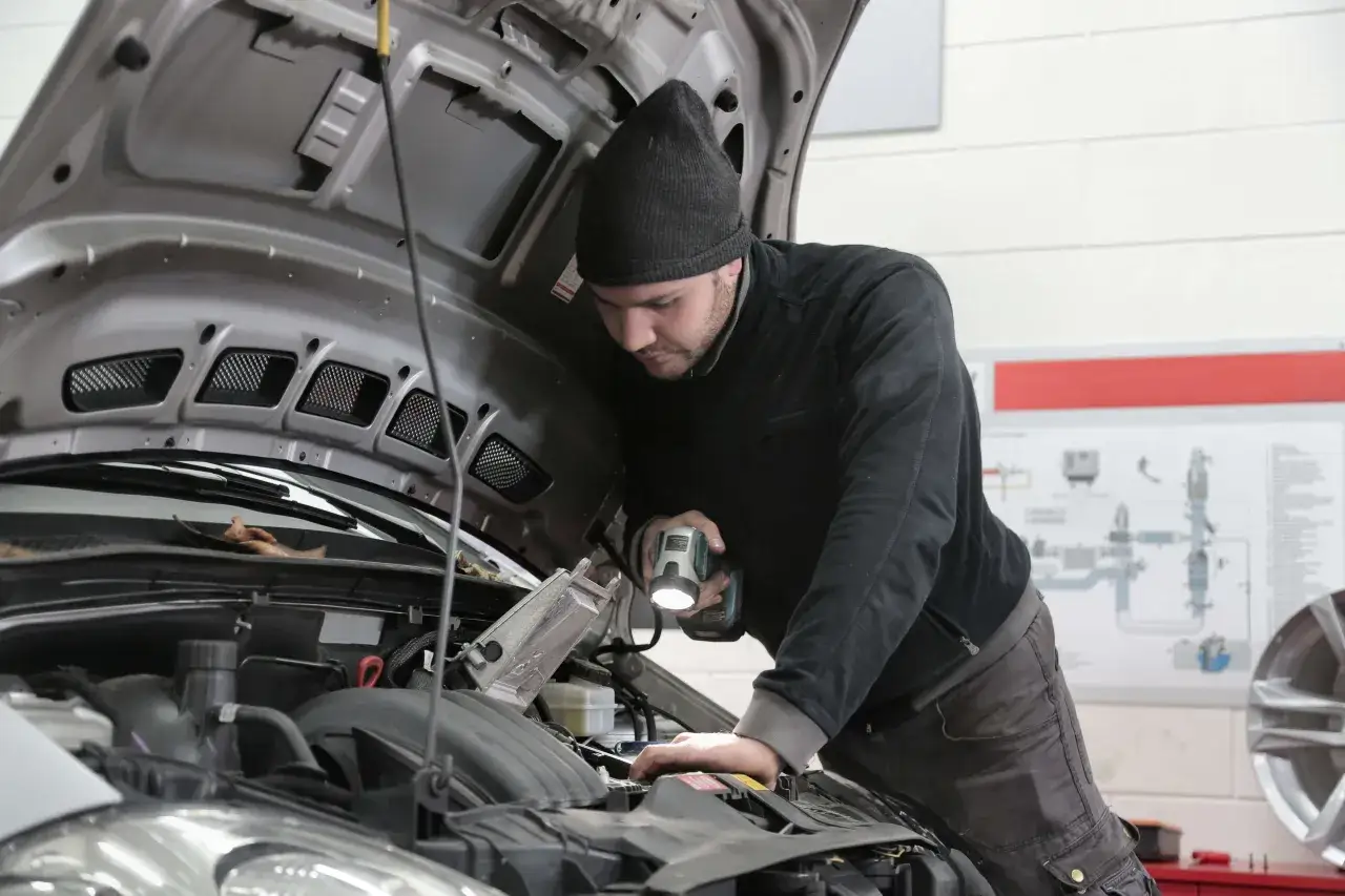 Mechanik z latarką sprawdza przegub w aucie.