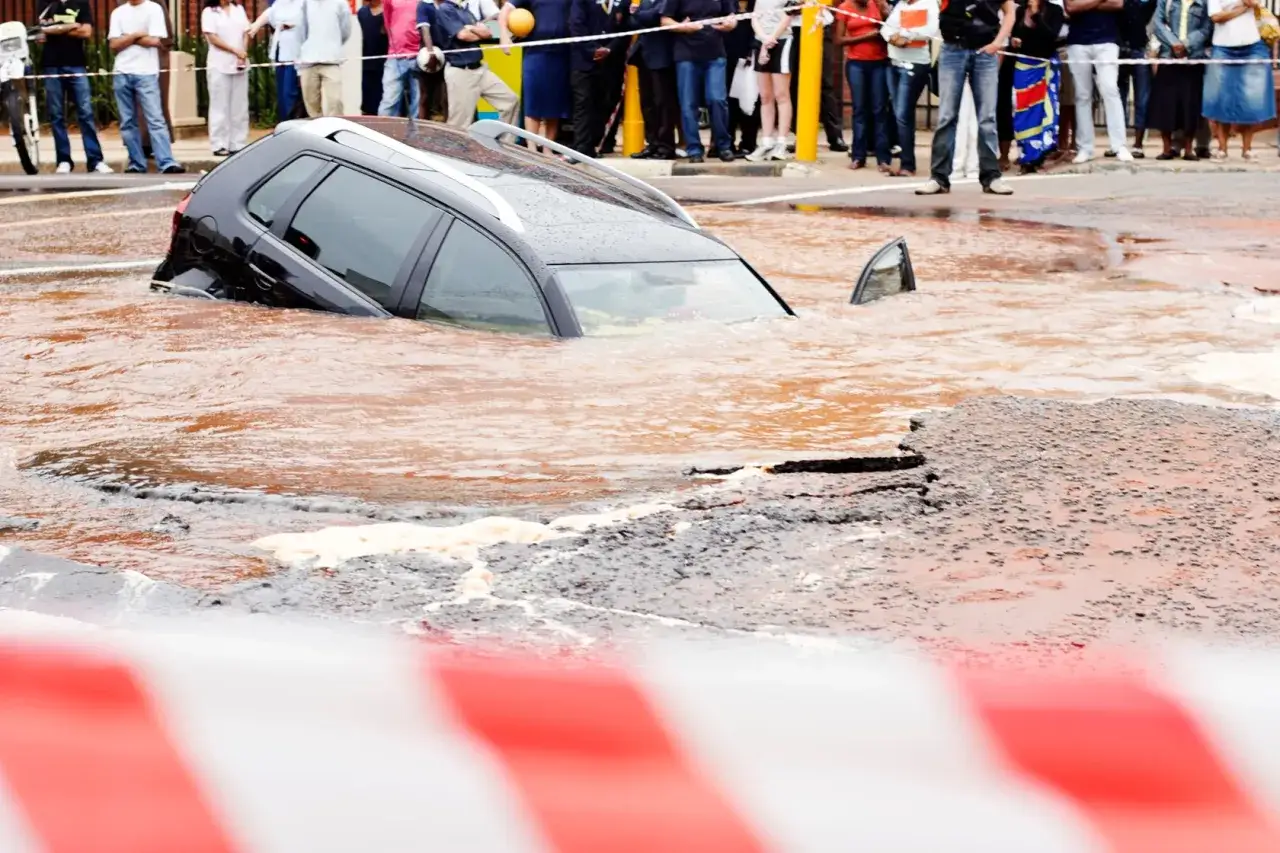 Czarny samochód tonie w brudnej wodzie po tym, jak kupiłem auto po powodzi. Ludzie obserwują z bezpiecznej odległości.