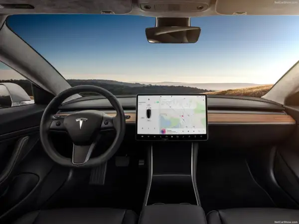 Wnętrze Tesla Model S z dużym ekranem dotykowym, kierownicą i widokiem na krajobraz za oknem.