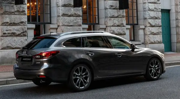 Eleganckie, ciemnoszare kombi Mazda 6, największe kombi na rynku, parkuje przed kamienną fasadą.
