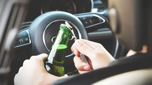 Ręce otwierają butelkę piwa za kierownicą. Nowe kary za jazdę po alkoholu powinny odstraszyć od takiego zachowania.