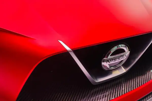 Czerwony Nissan z błyszczącym logo. To jaka to marka? Widać fragment maski i grill z włókna węglowego.