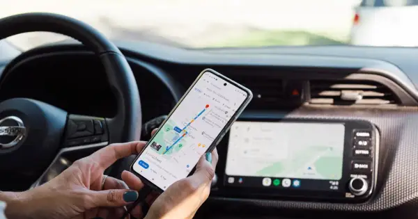 Ręce kierowcy trzymają telefon z nawigacją, co stanowi niebezpieczne używanie telefonu podczas jazdy.