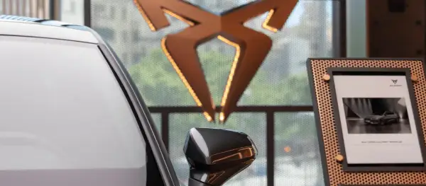 Biały samochód i logo producenta Cupra. Obok zdjęcie nowego modelu Cupra Leon PHEV.