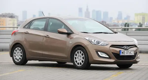 Brązowy Hyundai i30, jedna z popularnych generacji tego modelu, zaparkowany na tle miejskiej panoramy.