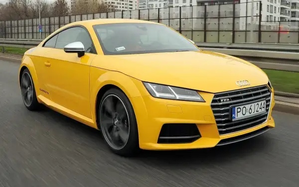 Żółte Audi TT RS, jedna z nowszych audi tt generacji, pędzi po drodze.